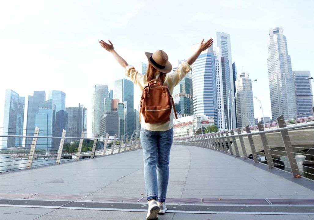Young woman traveler with backpack and hat traveling into Singapore city downtown. Travelling in Singapore concept.
