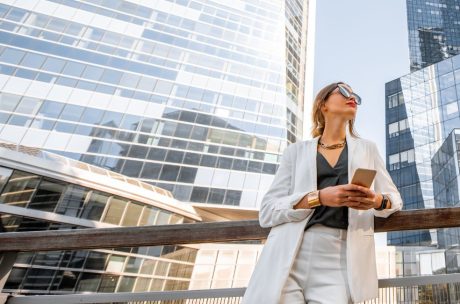 Woman standing with a mobile phone surrounded by tall buildings.