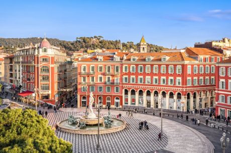 Statue in the town center with red buildings surrounding it.