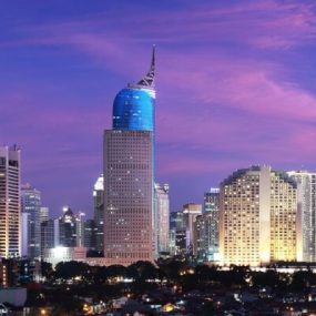 Jakarta, Indonesia featuring the Wisma 46 skyscraper, recognizable by its distinctive blue, pointed top, against a colorful twilight sky.