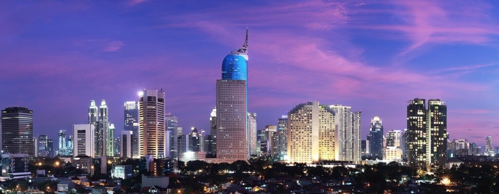 Jakarta, Indonesia featuring the Wisma 46 skyscraper, recognizable by its distinctive blue, pointed top, against a colorful twilight sky.