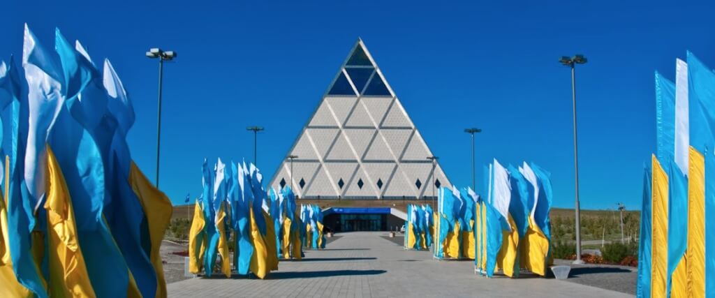 Palace of Peace and Reconciliation in Kazakhastan, a very distinctive pyramid-shaped building, with numerous blue and yellow flags leading up to it.