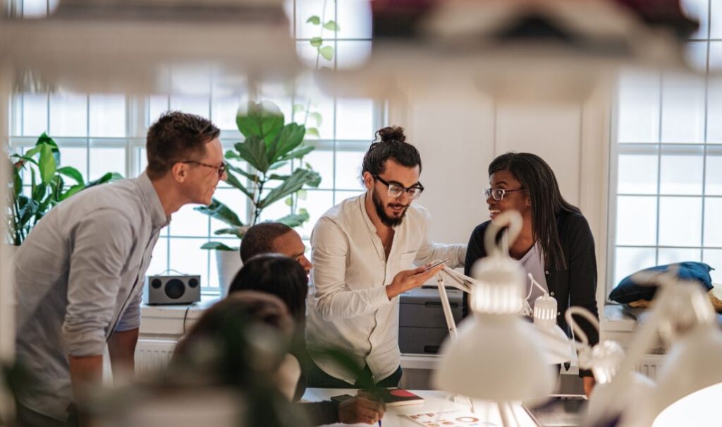 A group of coworkers gathered around a desk looking at a mobile phone.