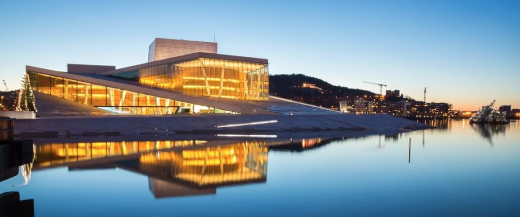Oslo, Norway, featuring the Oslo Opera House over calm waters, with city lights and hills in the background.