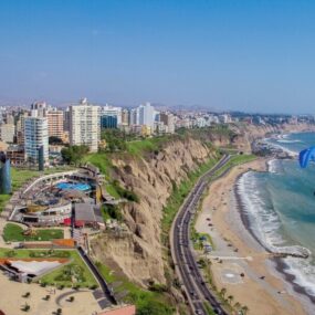 A park in Lima, Peru showcasing a cliffside park overlooking the Pacific Ocean, with modern buildings and a paraglider visible.