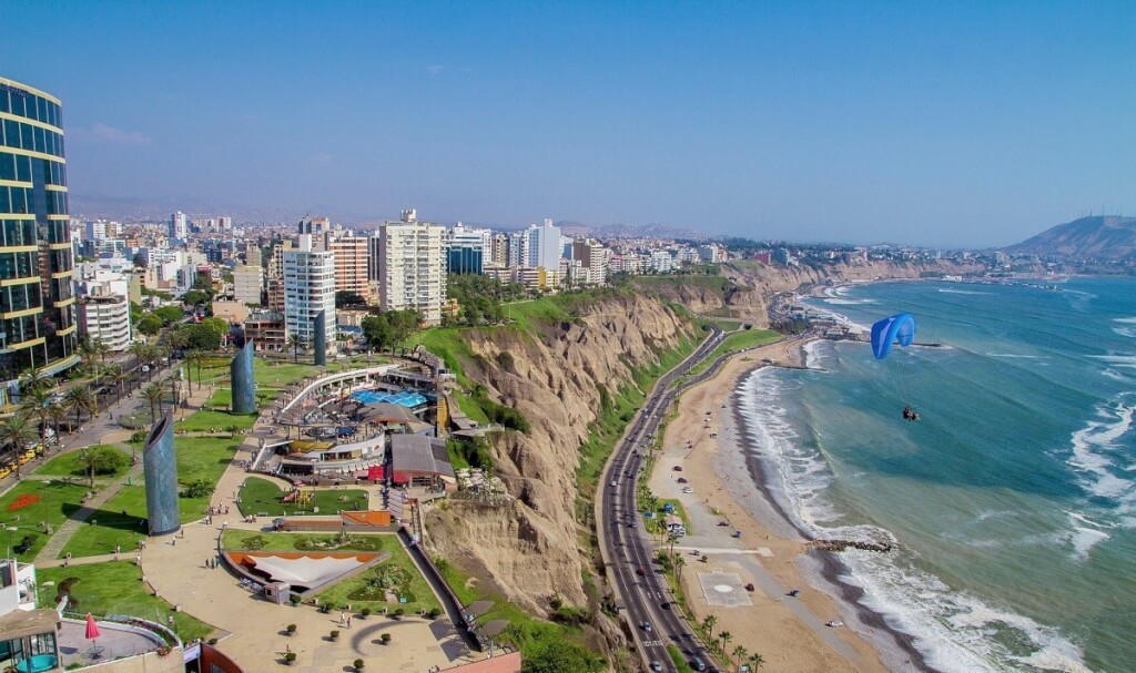 A park in Lima, Peru showcasing a cliffside park overlooking the Pacific Ocean, with modern buildings and a paraglider visible.