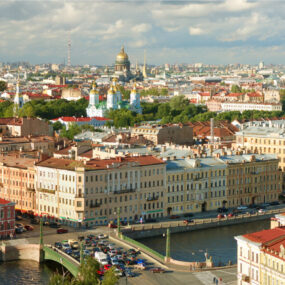 Saint Petersburg, Russia. It shows a cityscape with numerous historic buildings, a golden-domed cathedral, and a river with a bridge and cars.