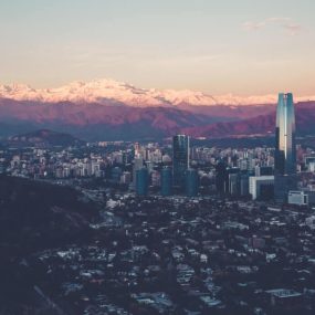 Santiago, Chile. It shows a sprawling cityscape with modern high-rise buildings against a backdrop of snow-capped mountains.