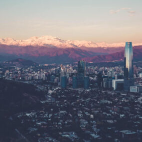 Santiago, Chile. It shows a sprawling cityscape with modern high-rise buildings against a backdrop of snow-capped mountains.
