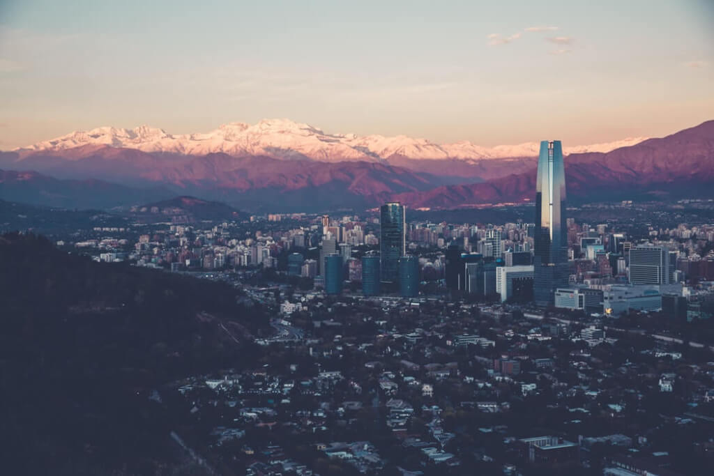 Santiago, Chile. It shows a sprawling cityscape with modern high-rise buildings against a backdrop of snow-capped mountains.