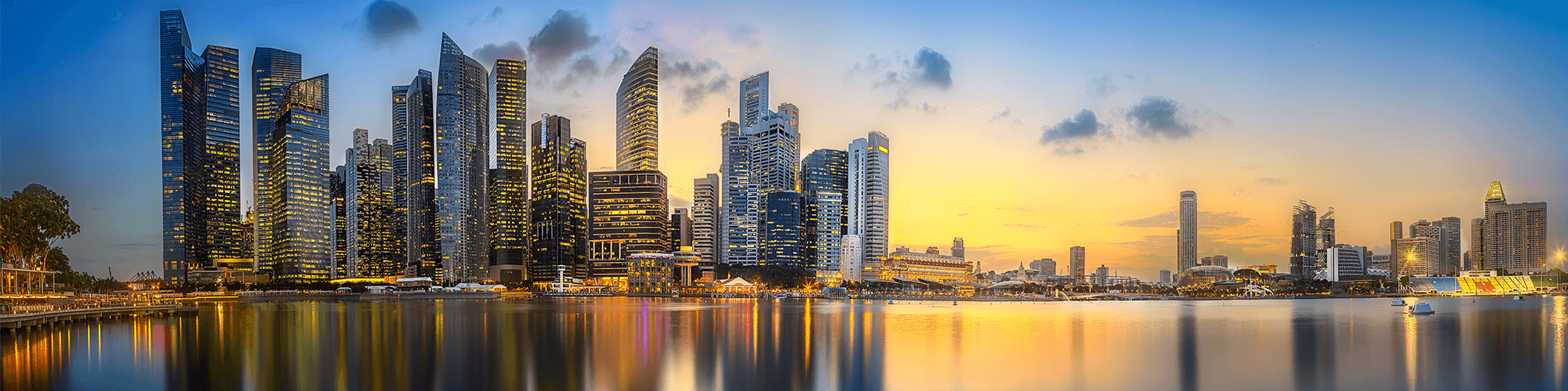 Singapore, It features a prominent skyline of modern skyscrapers reflected in the water, under a dramatic sunset or sunrise sky.
