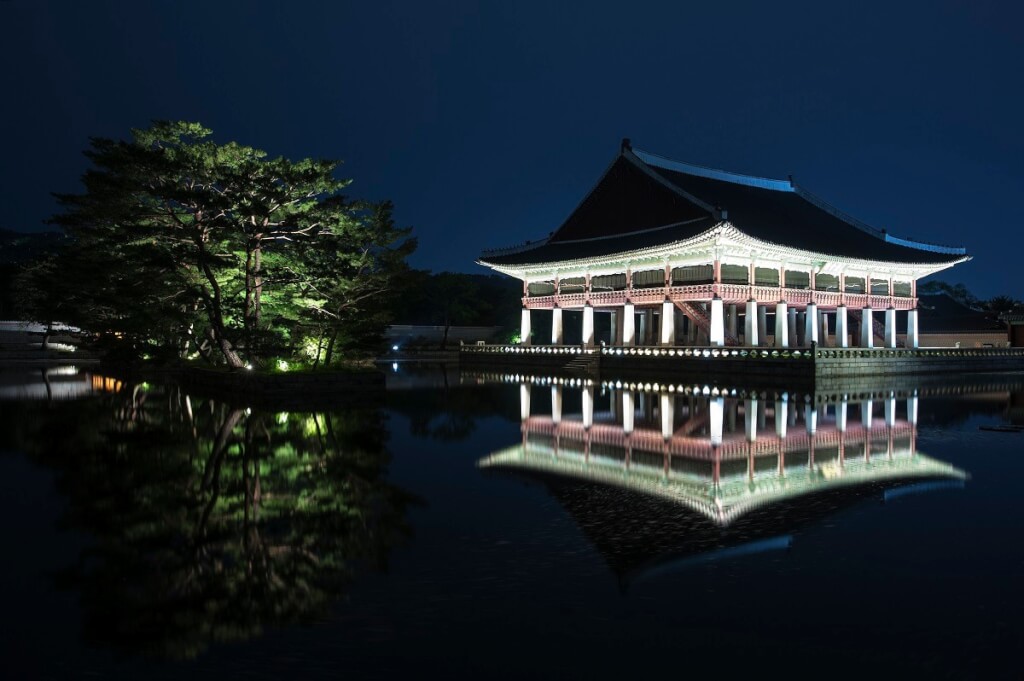 A palace in South Korea displayed in traditional Korean architectural style and reflection in a pond at night.