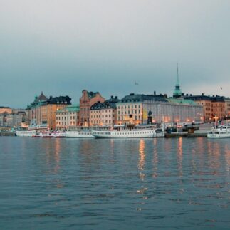 Sweden, features colorful historic buildings lining a waterfront with boats docked, under an overcast sky.