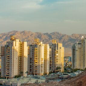 Cityscape in Afghanistan with tall residential buildings set against a backdrop of rugged mountains at sunset, highlighting the contrast between urban development and natural desert terrain.
