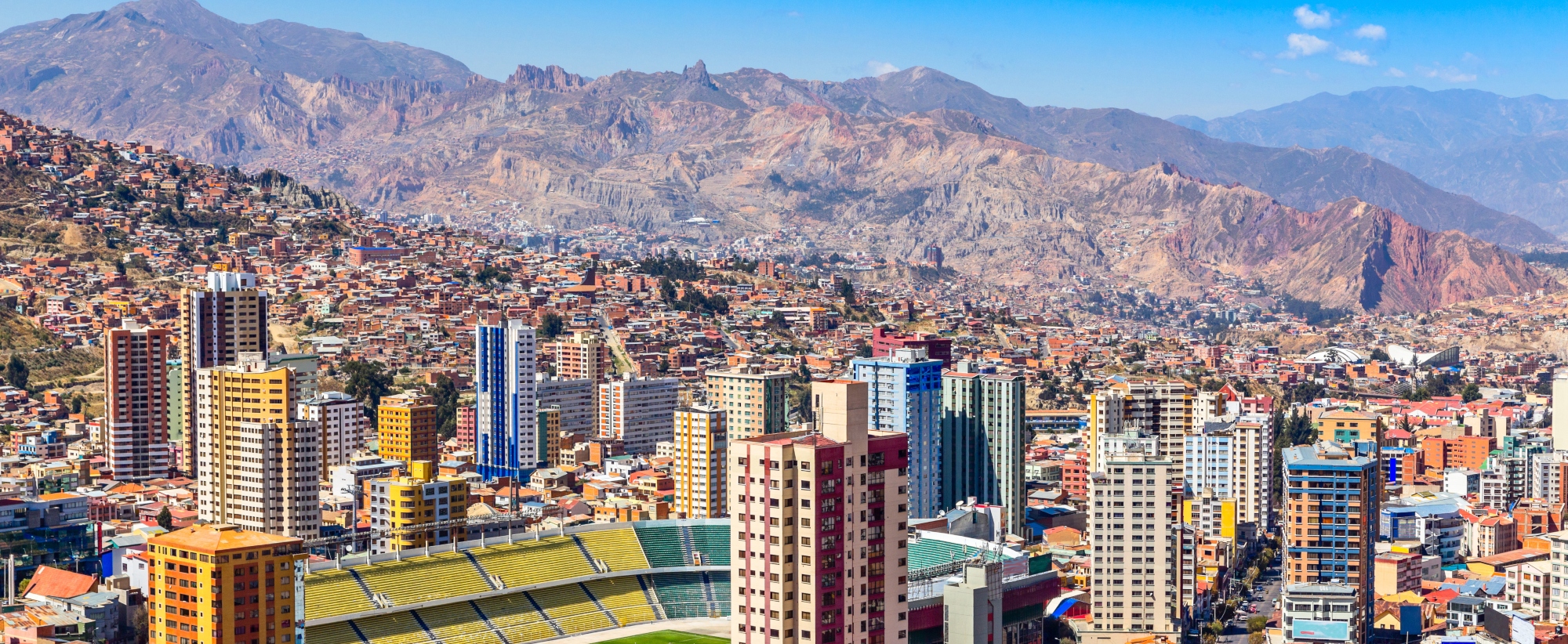Nuestra Senora de La Paz colorful city town center with skyscrapers, football stadium and lots of living houses scattered on the hills with Andes mountains in background, Bolivia.