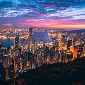 Panoramic view of Victoria Harbour and skyline of Hong Kong at dusk with the city lights illuminated and a colorful sky.