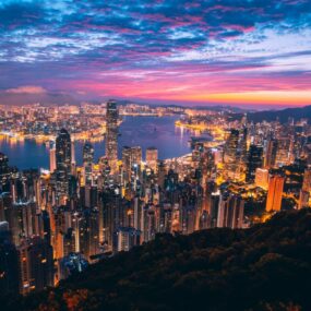 Panoramic view of Victoria Harbour and skyline of Hong Kong at dusk with the city lights illuminated and a colorful sky.