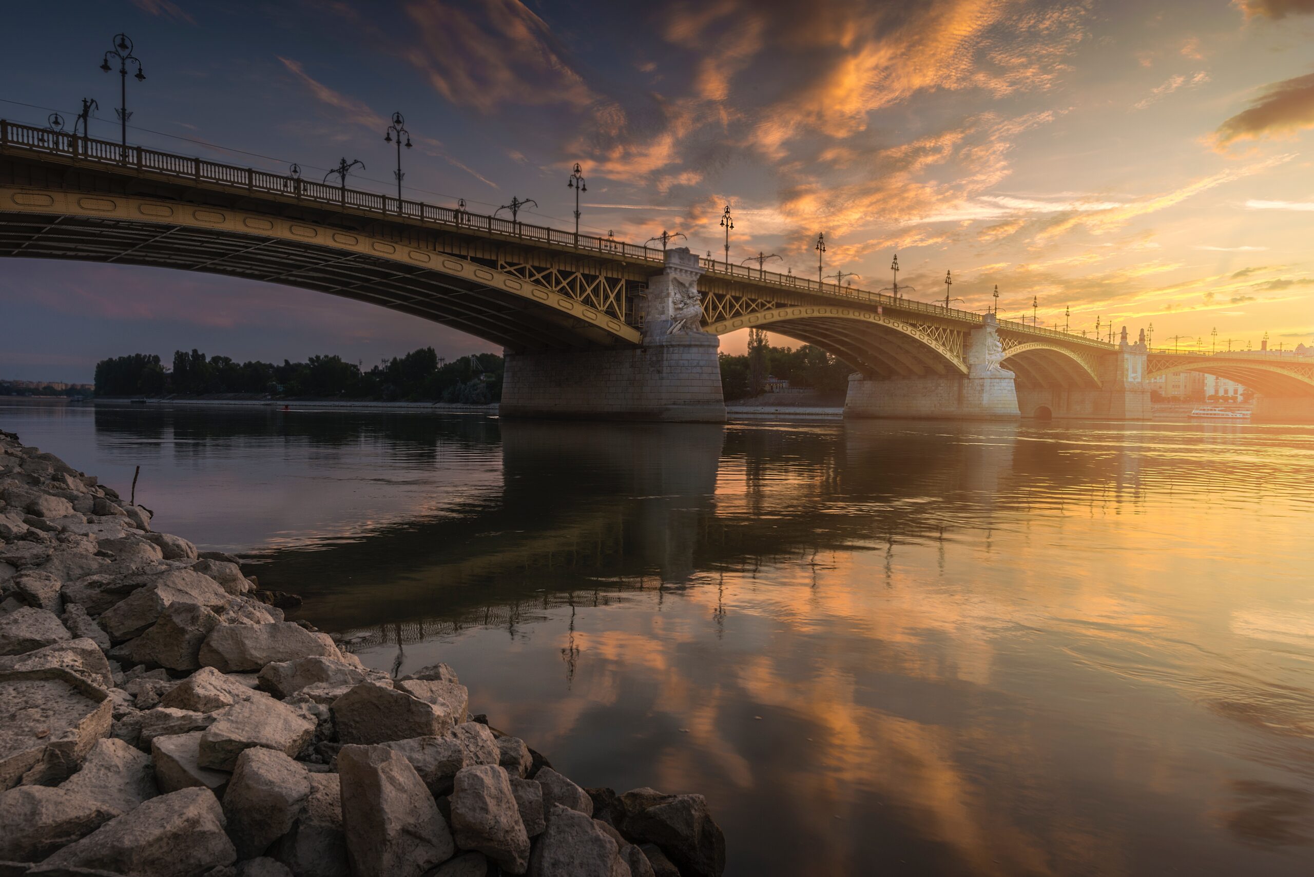 Margaret Bridge in Budapest, Hungary spanning the Danube River, with distinctive yellow color and lampposts during a beautiful sunset.