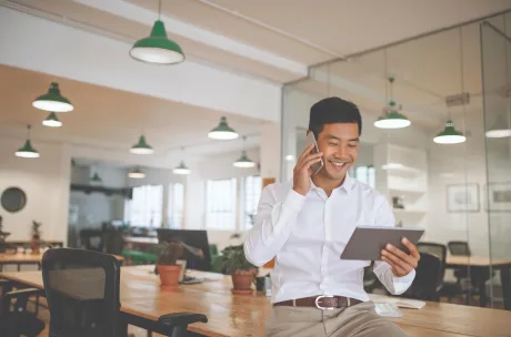 Man talking on a phone while looking at a tablet in a open workspace