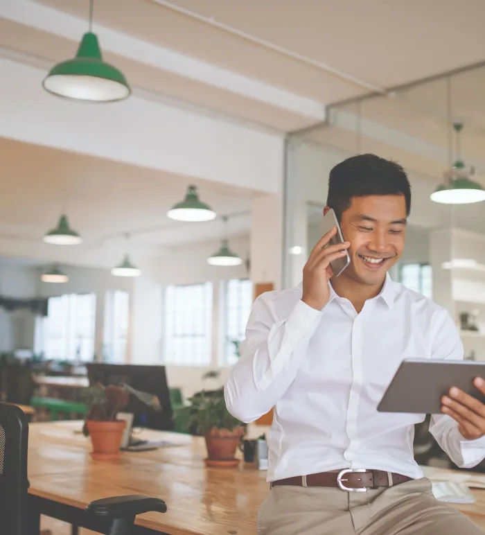 Man talking on a phone while looking at a tablet in a open workspace