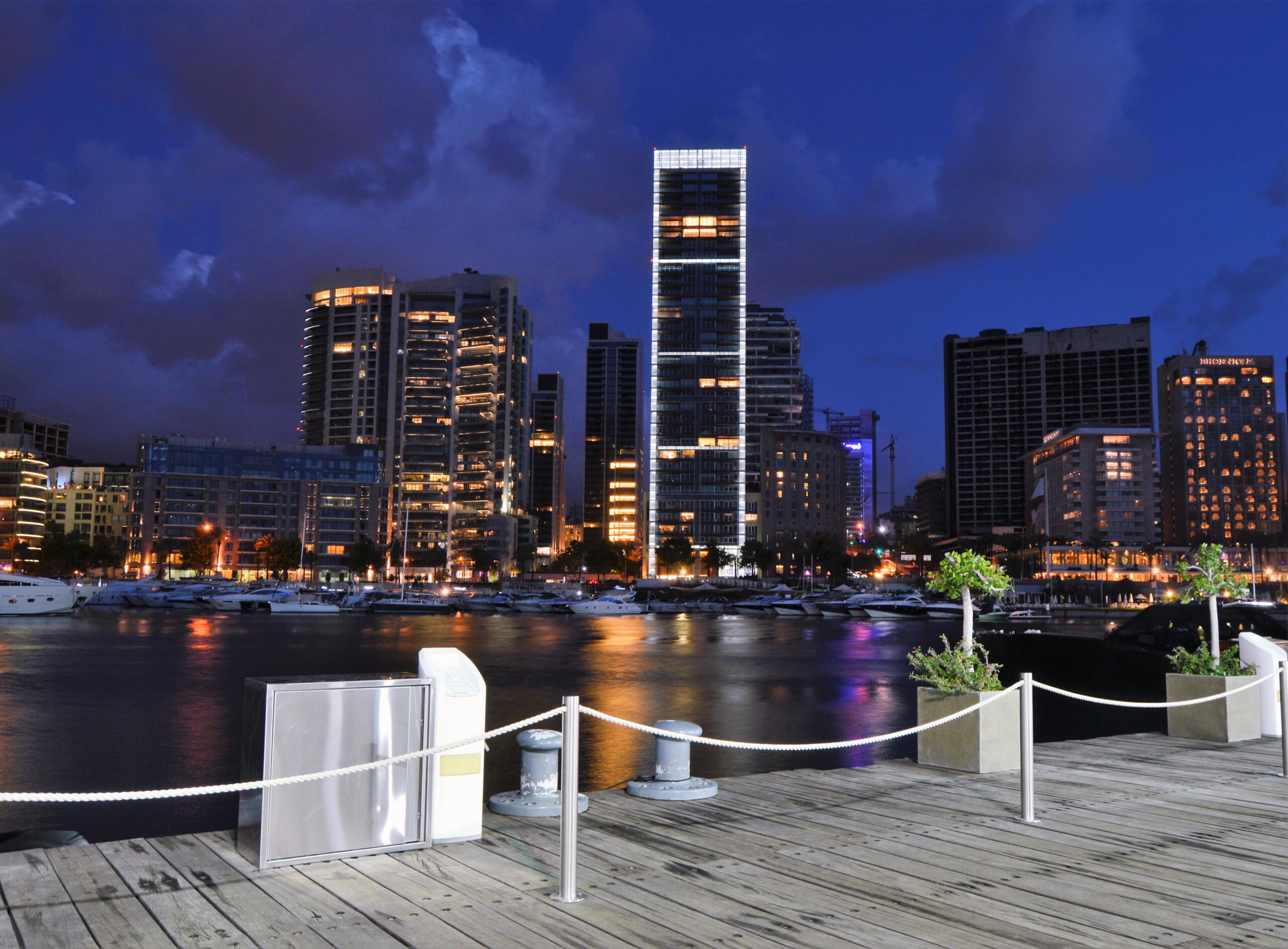 The modern skyline of Beirut, Lebanon, featuring a waterfront area with illuminated high-rise buildings and a marina at night.