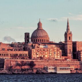 Malta's capital city with the dome and spire of the Carmelite Church and the Basilica of Our Lady of Mount Carmel, along with other historic limestone buildings, overlooking the Grand Harbour.