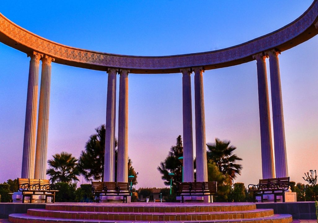 A monument in Pakistan featuring a series of columns arranged in a semi-circle, overlooking a landscaped area.