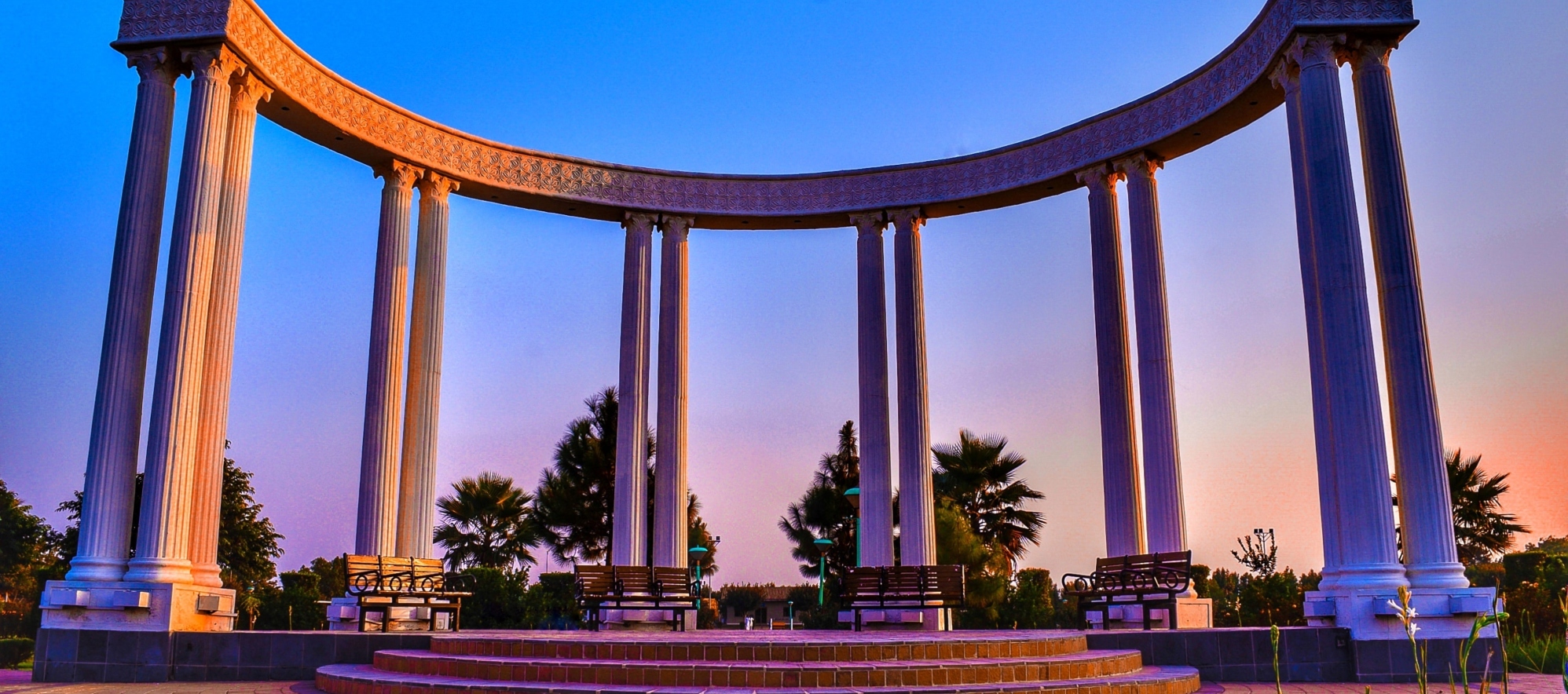 A monument in Pakistan featuring a series of columns arranged in a semi-circle, overlooking a landscaped area.
