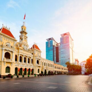 Historic colonial building with red roofs contrasts modern glass skyscrapers under a clear sky. Sunlight casts a warm glow, creating a serene atmosphere.