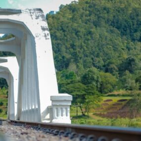 Zambia, a white bridge with arches over a railway track, surrounded by lush green hills under a bright sky.