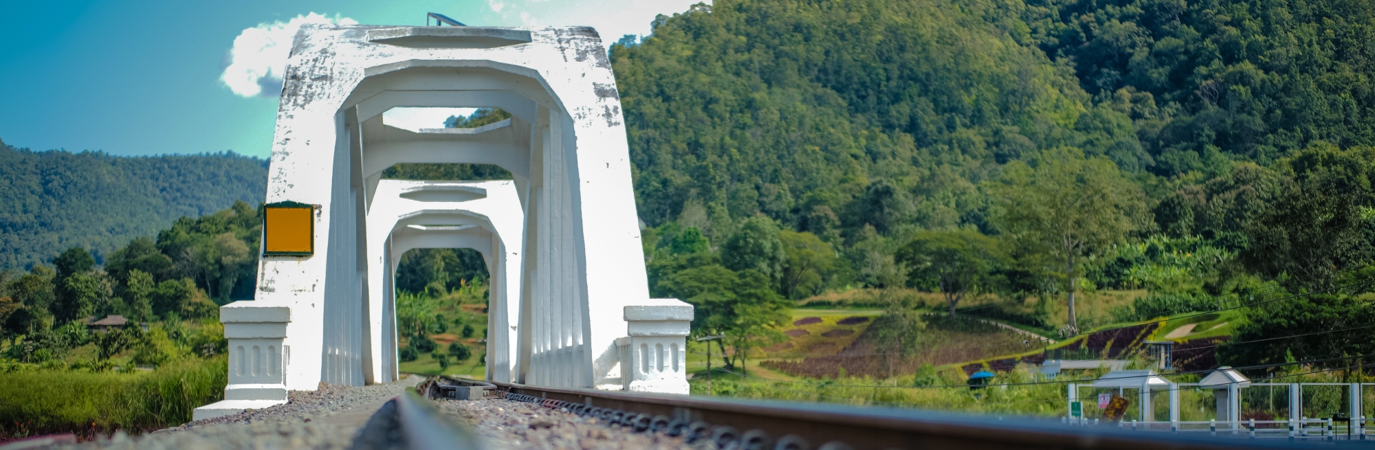 Zambia, a white bridge with arches over a railway track, surrounded by lush green hills under a bright sky.