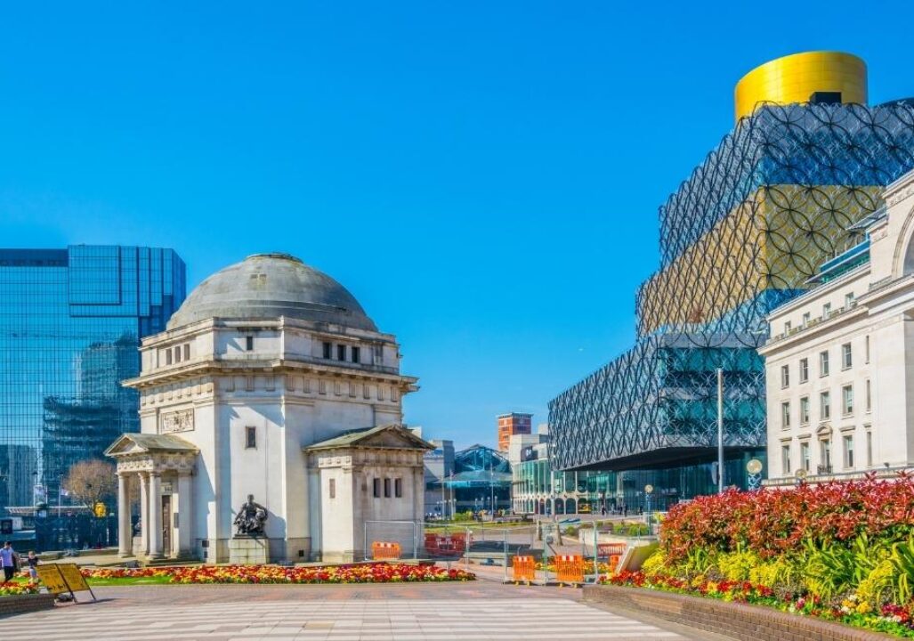A vibrant cityscape featuring a sunny day in Birmingham. Highlights include the classic domed Hall of Memory, modern Library of Birmingham, flowers, and blue sky.