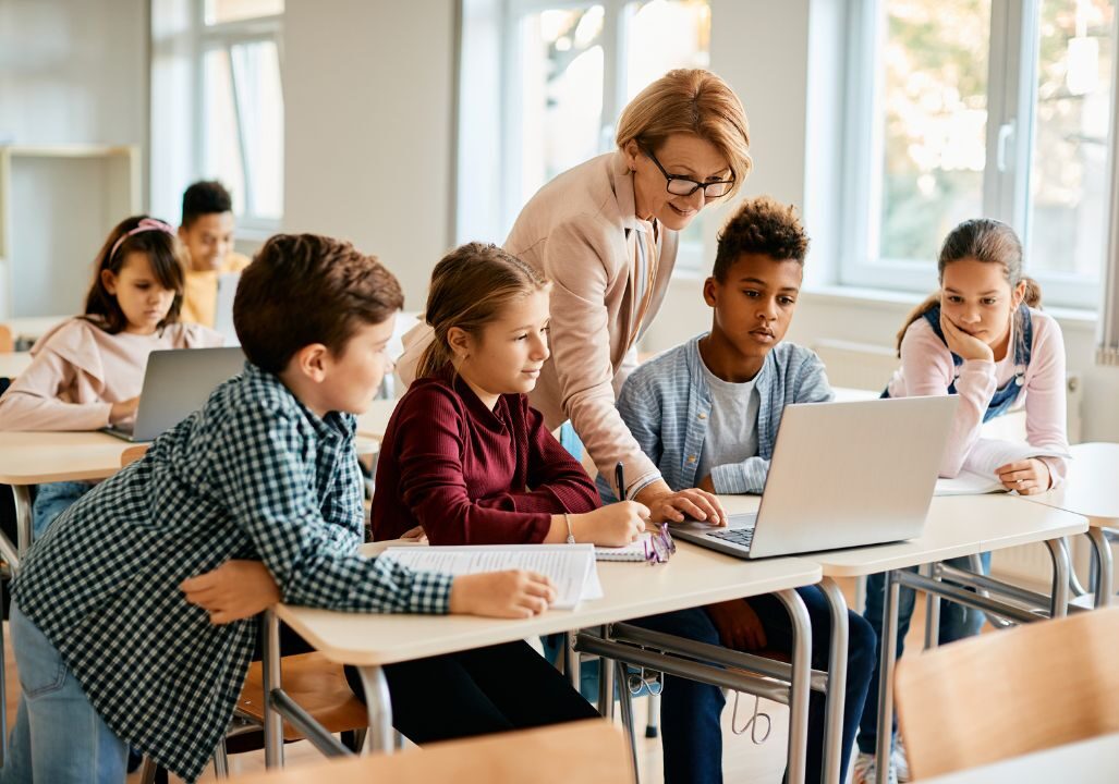 A group of elementary students having computer class with their teacher in classroom.