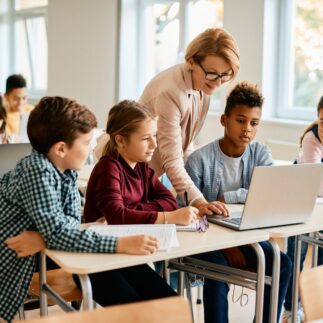 A group of elementary students having computer class with their teacher in classroom.