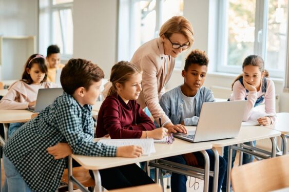 A group of elementary students having computer class with their teacher in classroom.